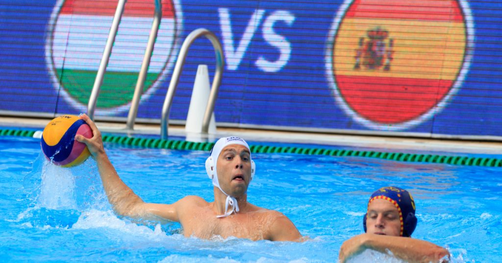  A water polo player in a white cap passes the ball past an opposing player in a red cap during a U14 Hungarian league match.